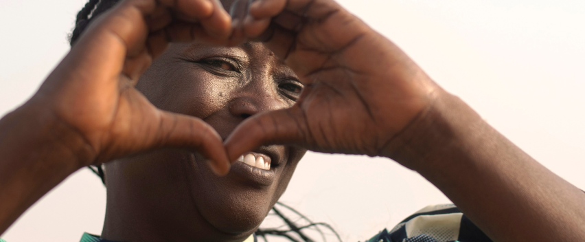 A young person making a heart shape with their hands over their eyes